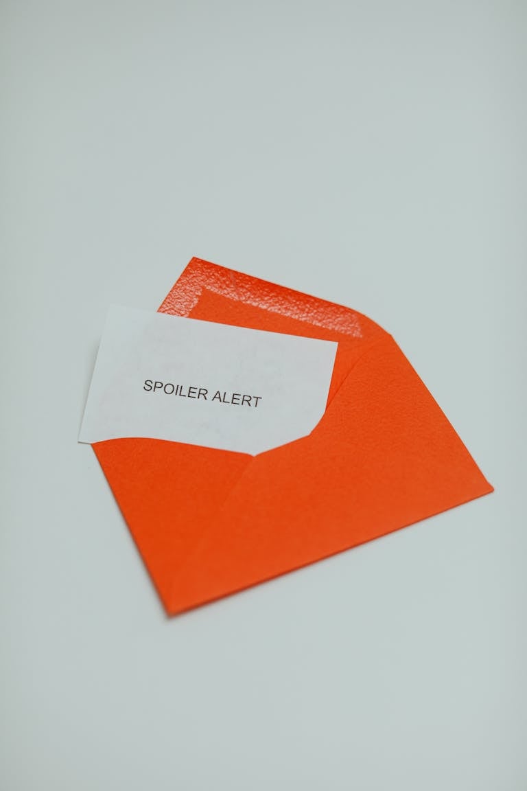 A minimalist photo of an open orange envelope with a white card displaying the text 'Spoiler Alert.'
